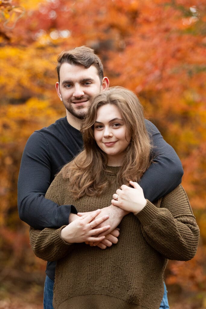 Engaged couple hugging from behind located at State Arboretum of Virginia